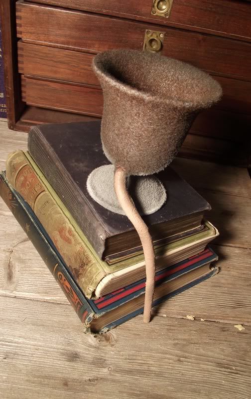 A fuzzy goblet style cup with a rat's tail sitting on top of a stack of books.